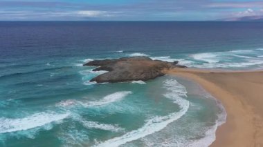 Cofete İslets 'in el değmemiş kıyı şeridinin sinematik hava görüntüsü canlı okyanus renklerini, engebeli dağları ve güneşli, bulutlarla dolu gökyüzünden gelen dinamik ışığı birleştiriyor..