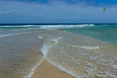 Sotavento Sahili 'nin kum tepesinde dinamik bir an. İki dalga karşılaşıp, altın kıyı şeridine yavaşça çarpıyor. Sahne, sakin turkuaz sularla gelgitin ritmi arasındaki zıtlığı yakalar..