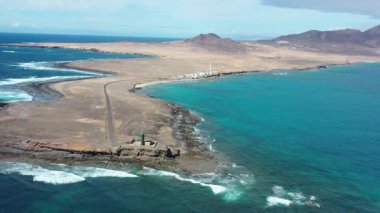 İnsansız hava aracı görüntüsü uzak Punta de Jandia Deniz Feneri 'ne giden manzaralı yolu gösteriyor. Jandia yarımadasının dramatik volkanik manzarasını vurguluyor..