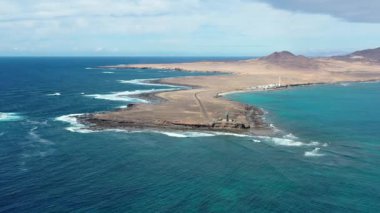 Punta de Jandia 'nın ikonik deniz fenerini görüntüleyen yüksek kaliteli bir hava görüntüsü. Kıyı manzarası ve çorak araziyi kesen ıssız bir yol..