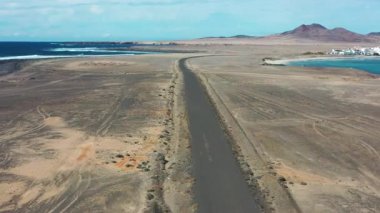Punta de Jandia 'ya giden uzak yolu ve güney Fuerteventura' nın engebeli manzarasına karşı kurulan El Puertito balıkçı köyünü kapsayan geniş bir drone perspektifi..