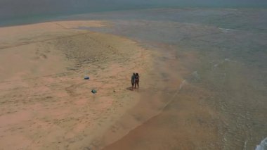 Playa de la Barca, Fuerteventura 'da Atlantik Okyanusu' yla çevrili bir kum dilinde huzurlu bir yürüyüşün keyfini çıkaran bir çiftin yukarıdan aşağıya bakan görüntüsü. Yaz tatili, doğa ve özgürlük.