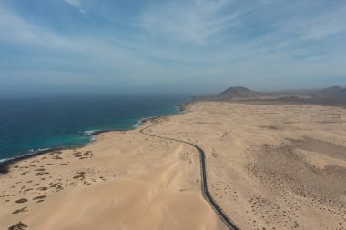 Corralejo Doğal Parkı, Fuerteventura 'da uzanan geniş altın kum tepeleri boyunca uzanan bir yol manzarası..