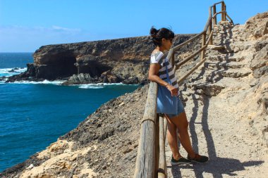 Fuerteventura 'daki Ajuy Mağaraları' na giden yolda uzanan bir kadın engebeli kıyı manzarasıyla çevrili huzurlu bir anın tadını çıkarıyor..