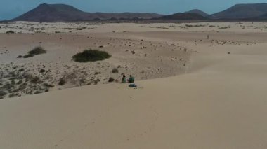 Romantik bir çiftin, Corralejo, Fuerteventura 'nın altın kum tepelerinde birlikte oturup engin bir doğal manzarayla çevrili huzurlu bir anın tadını çıkarışının havadan görüntüsü..