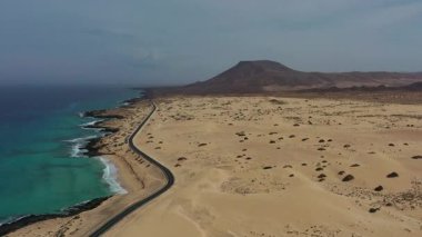 Corralejo kumullarını geçen ikonik yolun sinematik hava görüntüleri, Kanarya Adaları 'nın eşsiz volkanik manzarasını ve güneşli havasını vurguluyor..