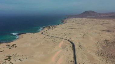 Corralejo kumullarını geçen ikonik yolun sinematik hava görüntüleri, Kanarya Adaları 'nın eşsiz volkanik manzarasını ve güneşli havasını vurguluyor..