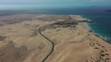 Fuerteventura, Kanarya Adaları 'ndaki Corralejo Doğal Parkı' nın insansız hava aracı görüntüleri, altın kum tepeleri, turkuaz okyanus ve arka planda bir otel. Seyahat, turizm, doğa ve tatil kavramları için ideal.