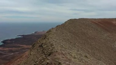Fuerteventura, Kanarya Adaları 'ndaki Montaa Roja zirvesine giden dar sırtın hava aracı görüntüleri. Volkanik arazi, kırmızı kayalar, dramatik yükseliş, macera ve uzak bir çevrede doğa manzarası.