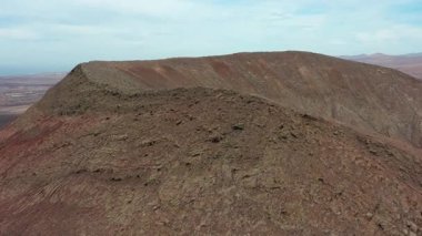 Fuerteventura, Kanarya Adaları 'ndaki Montaa Roja zirvesine giden dar sırtın hava aracı görüntüleri. Volkanik arazi, kırmızı kayalar, dramatik yükseliş, macera ve uzak bir çevrede doğa manzarası.