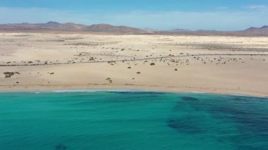 Güneşli bir günde Corralejo Çölü 'nün yanındaki El Rosadero Sahili' nden geçen düz bir otoyolun hava görüntüsü. Hareket halindeki arabalar, altın kum tepeleri ve Atlantik kıyıları Fuerteventura, Kanarya Adaları 'ndan gelen bu insansız hava aracı videosunda çarpıcı bir kontrastlık yaratıyor..