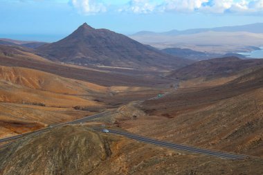 Fuerteventura 'nın çorak, güneşli manzarasında eğri büğrü bir dağ geçidinin göz kamaştırıcı manzarası..