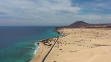 Kanarya Adaları, Fuerteventura 'daki Corralejo' nun engin kum tepelerini kesen ıssız bir yolun yüksek kaliteli hava aracı görüntüleri. Sahne hareketi, ölçeği ve kontrastı vurguluyor. Yol, el değmemiş kumul manzarasını aydınlık altında bölüyor.