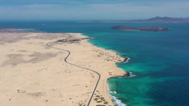 Corralejo, Fuerteventura, Kanarya Adaları 'ndan geçen hava aracı görüntüleri. Video, sahil yolunun uzun bir bölümünü ve arka planda açık gökyüzü altında bulunan Lobos ve Lanzarote adalarını gösteriyor..