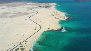 Kanarya Adaları, Fuerteventura 'daki Corralejo' nun engin kum tepelerini kesen ıssız bir yolun yüksek kaliteli hava aracı görüntüleri. Sahne hareketi, ölçeği ve kontrastı vurguluyor,