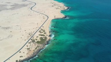Kanarya Adaları, Fuerteventura 'daki Corralejo' nun engin kum tepelerini kesen ıssız bir yolun yüksek kaliteli hava aracı görüntüleri. Sahne hareketi, ölçeği ve kontrastı vurguluyor. Yol, el değmemiş kum manzarasını bölüyor.