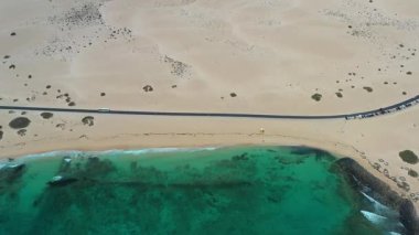 Corralejo doğal parkının insansız hava aracı görüntüleri geniş çöl kumullarını, kıyı plajlarını ve Kanarya Adaları 'ndaki Fuerteventura volkanik arazisini kesen yolu gösteriyor..