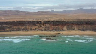 Bulutlu bir günde Fuerteventura 'daki uzak bir plajın insansız hava aracı görüntüleri, doğayı, seyahatleri ve kıyı manzaralarını temsil ediyor..