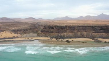 Esquinzo Sahili 'nin yüksek açılı görüntüsü dramatik bulutlar ve turkuaz okyanus suları içeriyor..