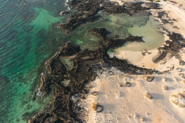 Gün batımında Fuerteventura 'daki El Islote Sahili' nin insansız hava aracı fotoğrafı volkanik kumlarda, dramatik ışıkta, Atlantik kıyılarında ve sakin ada atmosferinde geleneksel dairesel rüzgar sığınaklarını gösteriyor..