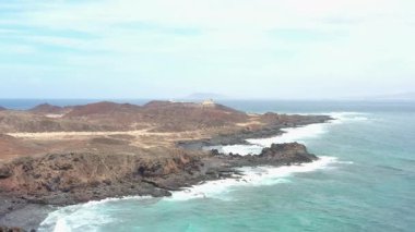 Punta Martino Deniz Feneri 'nin arka planında İspanya' nın Kanarya Adaları 'nın bulunduğu Lobos Adası' nın engebeli kıyı şeridinin insansız hava aracı görüntüleri. Volkanik uçurumlar, turkuaz sular ve uzak ada doğasının yer aldığı Atlantik manzaralı deniz manzarası.