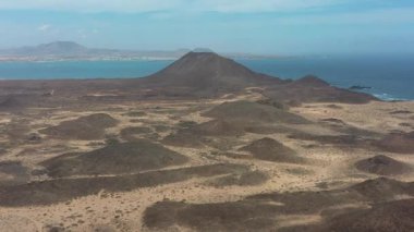 İspanya 'nın Kanarya Adaları' nda Montana de La Caldera ile Isla de Lobos 'un kurak volkanik manzarasının hava aracı görüntüleri. Lav tarlaları ve uzak ada doğası olan manzaralı çöl arazisi..