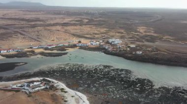 Bulutlu bir günde Majanicho kıyılarının panoramik drone görüntüleri. Derin mavi okyanus ve Kuzey Fuerteventura 'daki kuru volkanik manzara arasındaki zıtlık. Sahil kıyısındaki geleneksel Kanarya Adaları evleri. Huzurlu ve seyrek nüfuslu.