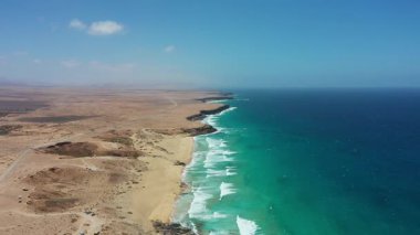 Uçurtmacıların ve sörfçülerin tepeden aşağı görüntüsü Playa del Castillo, Fuerteventura, Kanarya Adaları, İspanya 'da rüzgarlı havanın tadını çıkarıyor. Atlantik Okyanusu 'nun üzerindeki canlı uçurtmalar bu manzaralı kıyı manzarasındaki altın plajla tezat oluşturuyor..