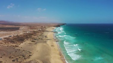 Uçurtmacıların ve sörfçülerin tepeden aşağı görüntüsü Playa del Castillo, Fuerteventura, Kanarya Adaları, İspanya 'da rüzgarlı havanın tadını çıkarıyor. Atlantik Okyanusu 'nun üzerindeki canlı uçurtmalar bu manzaralı kıyı manzarasındaki altın plajla tezat oluşturuyor..
