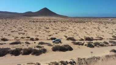 Kanarya Adaları 'ndaki Fuerteventura çölünde ilerleyen 4x4' lük bir aracın hava aracı görüntüsü engebeli manzaralar, tozlu patikalar ve uzak doğal manzaralar sergiliyor..