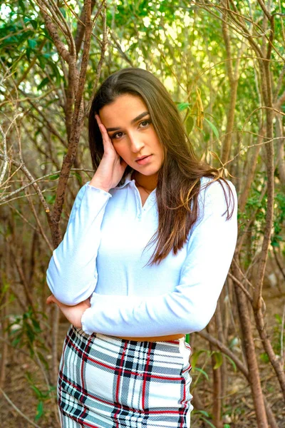 Una mujer seria mirando desde detrás del árbol. Mujer bastante tranquila tocando el árbol y mirando a la cámara en el bosque tranquilo — Foto de Stock