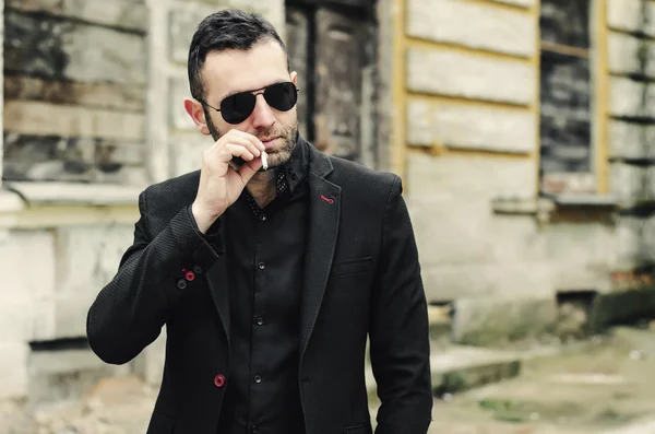 Guapo elegante joven fumando fuera en un entorno urbano — Foto de Stock