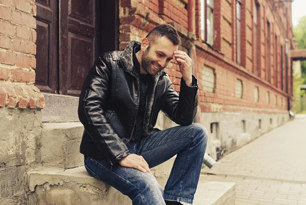 A handsome man with beard sitting on steps outside wearing a  je — Stock Photo, Image