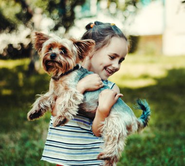çizgili kazaklı küçük kız gülümsüyor ve küçük bir köpek tutar