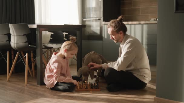一个小女孩和她的父亲正在厨房里下棋 坐在地板上 附近站着一只狗 斯堪的纳维亚和高科技风格在内地 家庭休闲 — 图库视频影像