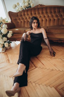 Siyah elbiseli şık bir manken kanepenin yanında oturuyor.