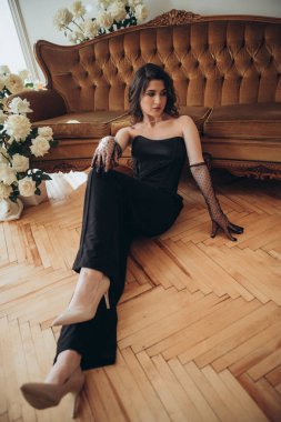 Siyah elbiseli şık bir kadın çıplak ayakla oturuyor.