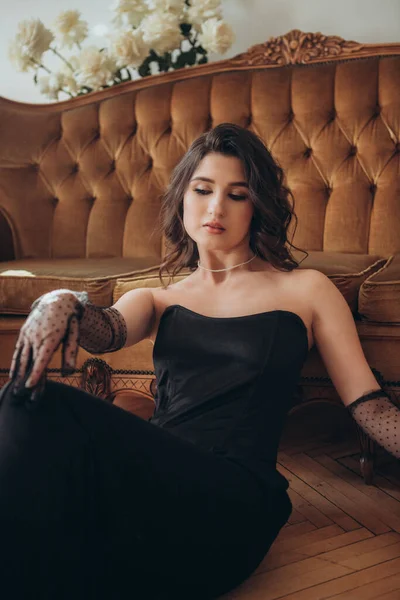 Siyah elbiseli zarif kadın kanepede dinleniyor.