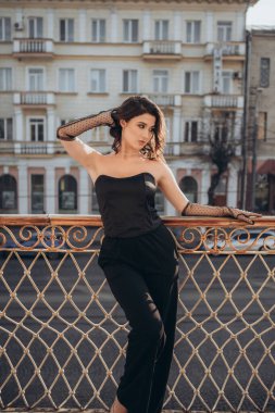 Siyah elbiseli, balkonda poz veren büyüleyici kadın.