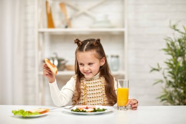 Küçük kız kahvaltı yapıyor. Yağda yumurta ve portakal suyu.