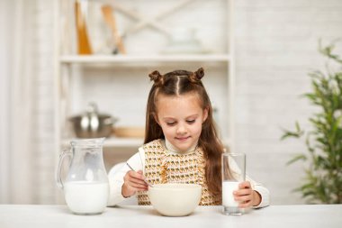 Küçük kız kahvaltı yapıyor: mısır gevreği ve mutfakta süt..