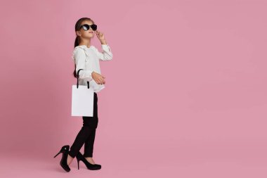 Güneş gözlüklü kız alışveriş torbaları tutuyor.