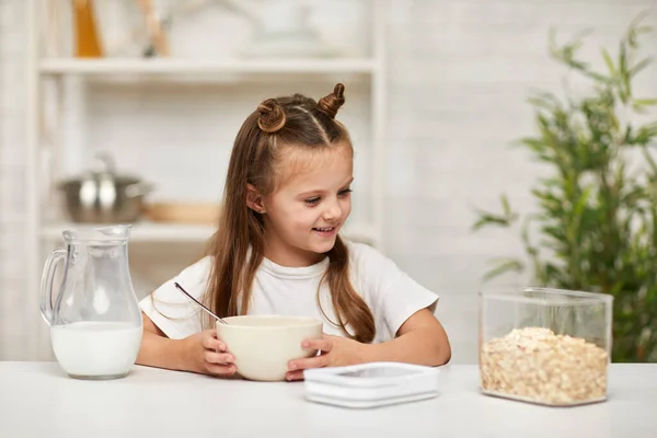 Маленька дівчинка їсть сніданок: крупа з молоком на кухні . — стокове фото