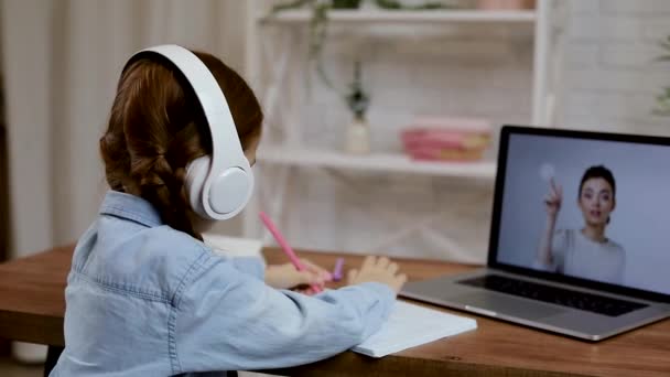 Niña pequeña usando el ordenador portátil para hacer tareas escolares en casa y escribir notas. — Vídeos de Stock
