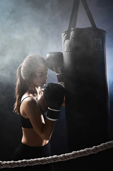 Woman in black boxing gloves leaning on punching bag — Stock Photo, Image