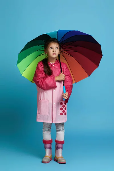 Pembe yağmurluklu, çok renkli şemsiyeli çocuk. — Stok fotoğraf
