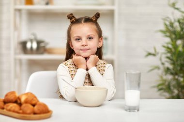 Küçük kız kahvaltı yapıyor: mısır gevreği ve mutfakta süt..