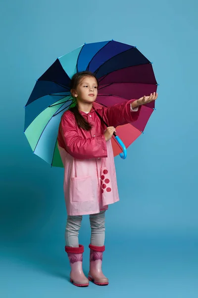 Pembe yağmurluklu, çok renkli şemsiyeli çocuk. — Stok fotoğraf