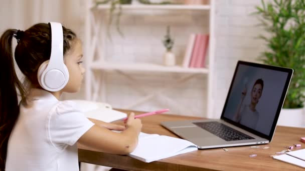 Lille barn pige ved hjælp af bærbar computer til at gøre skoleopgaver derhjemme og skrive noter. – Stock-video