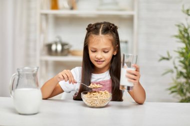 Küçük tatlı kız kahvaltı yapıyor: mısır gevreği ve süt.